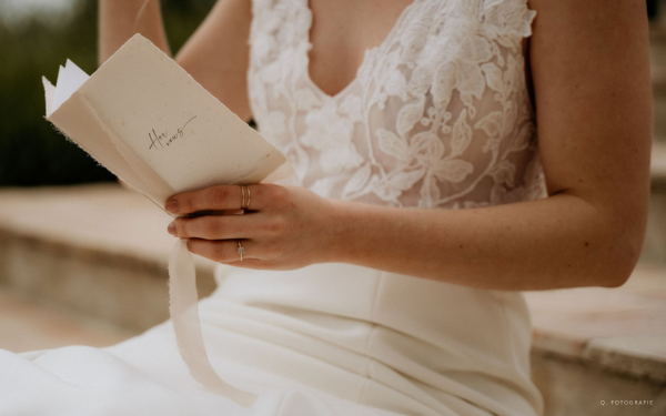 Bruid met kanten trouwjurk aan met geloftenboekje van handgeschept papier in haar hand waarop staat her vows.